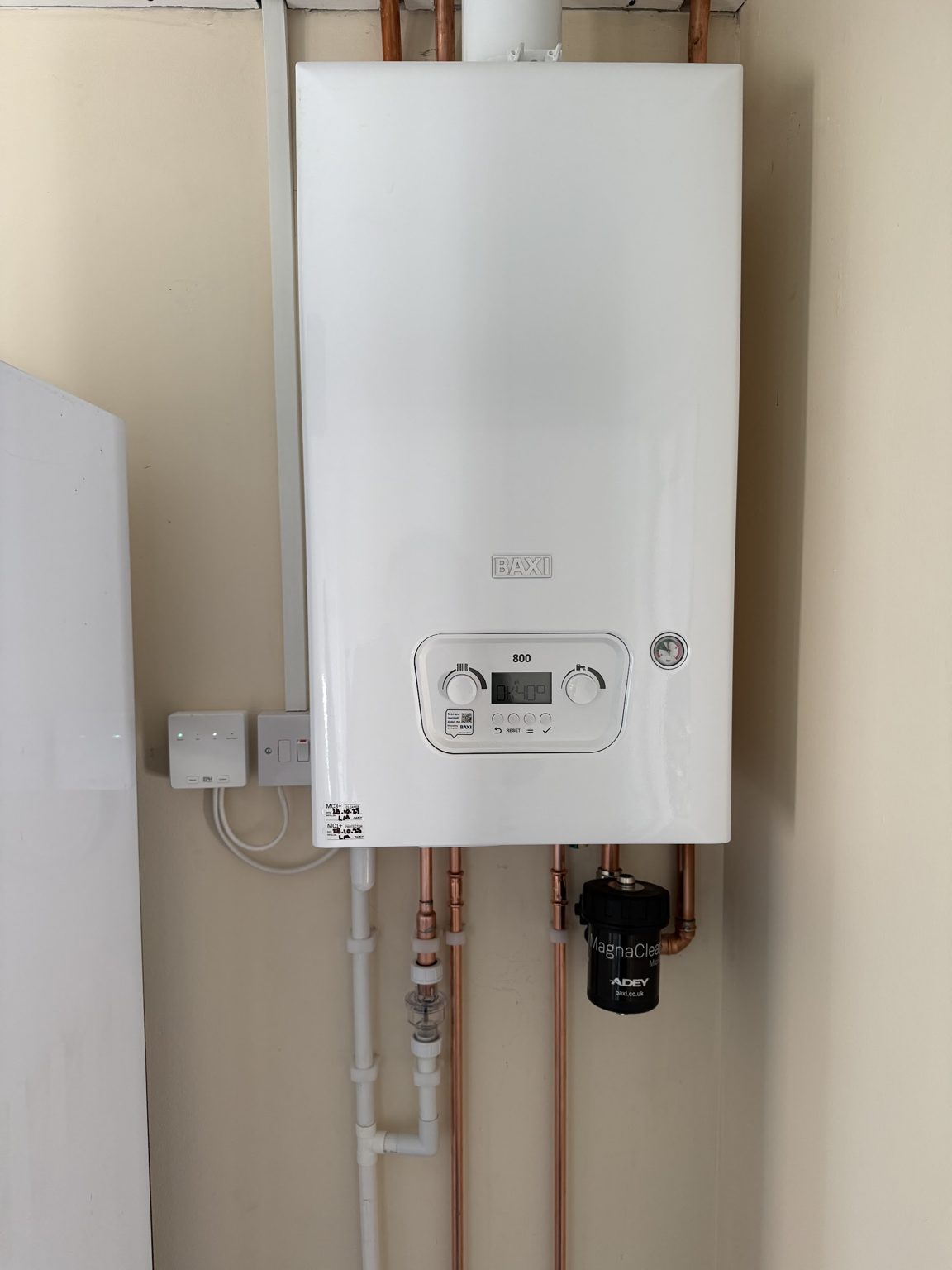 A new combi boiler on the wall with copper pipework and a magnetic filter below