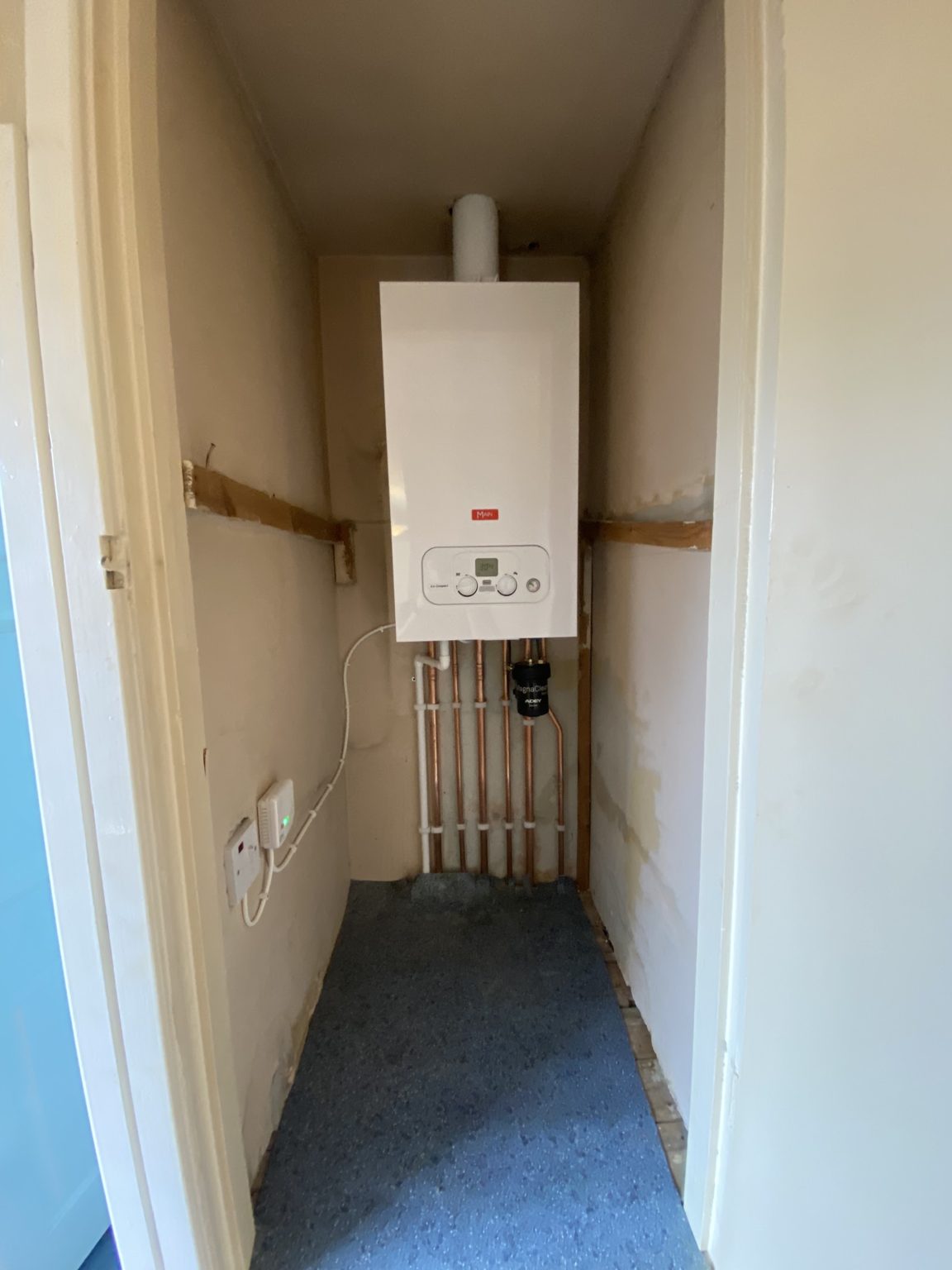 A new boiler fitted at the end of a narrow cupboard, pipework run neatly below